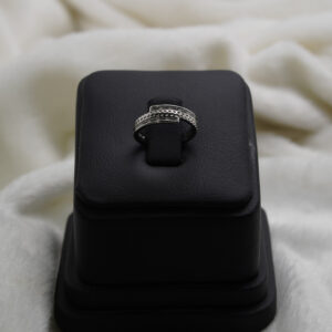A silver double band ring displayed on nleaher stand featuring a sleek geomatric design with small embedded stones and a polished finish